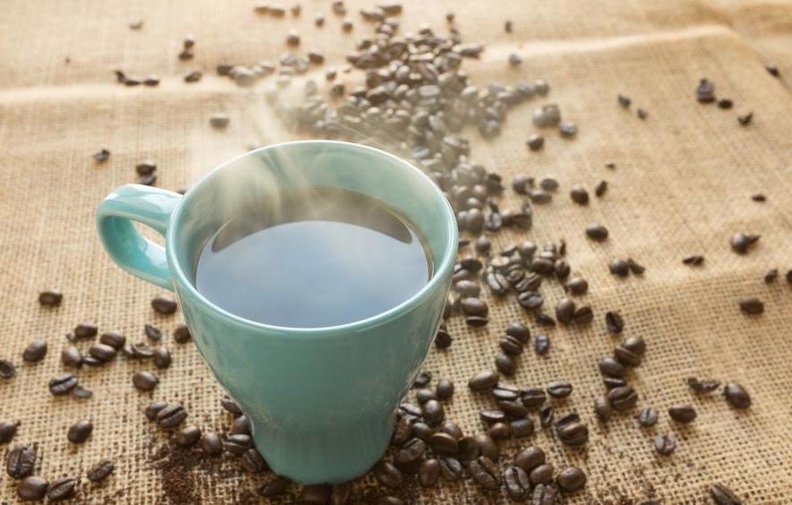 turqyoise coffee cup with coffee steaming hot in it and coffee beans spilled on the table top